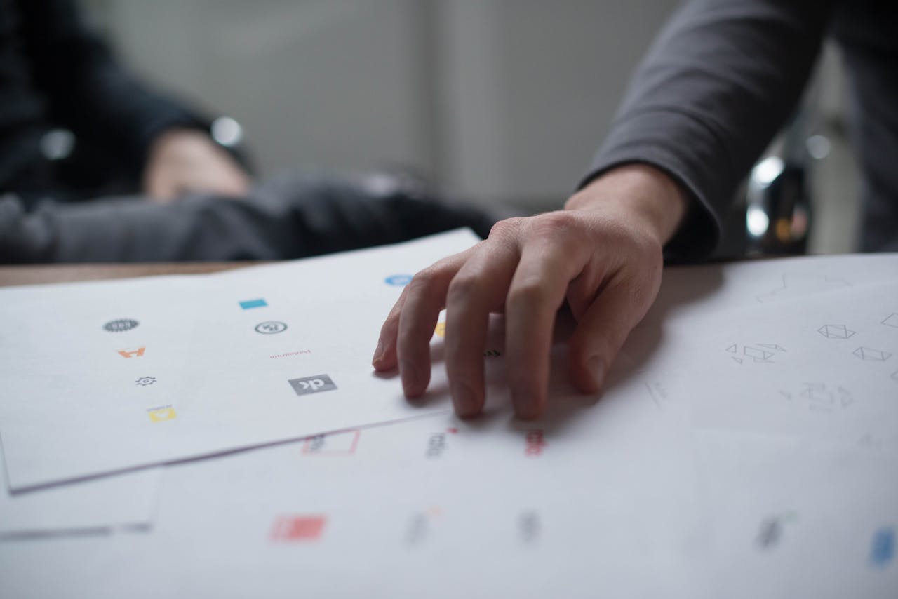 heros-img A close-up shot of a hand reviewing various logo designs on paper, ideal for business concepts.